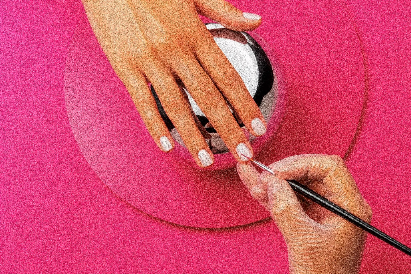 A nail tech painting a client’s nail with a fine brush, on a fuchsia background