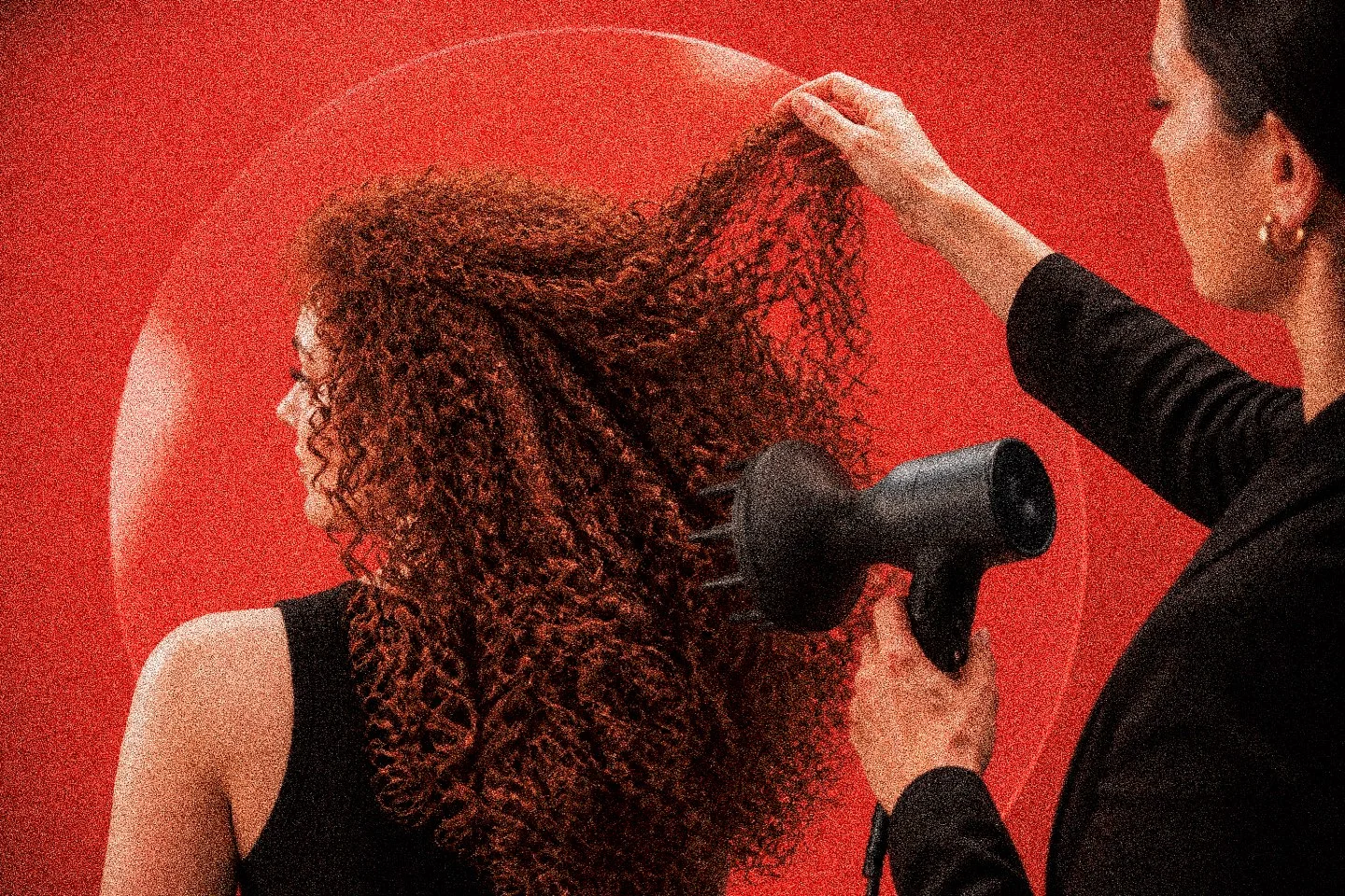 A stylist drying curls with a diffuser, under red light